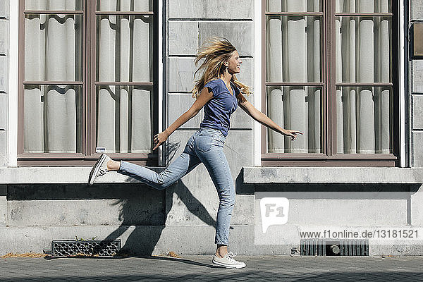 Niederlande  Maastricht  glückliche blonde junge Frau rennt an einem Gebäude in der Stadt entlang