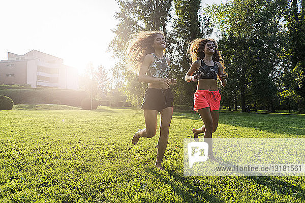 Zwillingsschwestern joggen barfuss auf einer Wiese