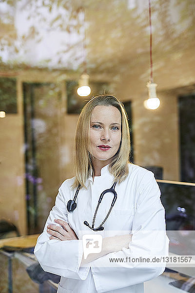 Porträt einer Ärztin mit Stethoskop hinter einer Fensterscheibe