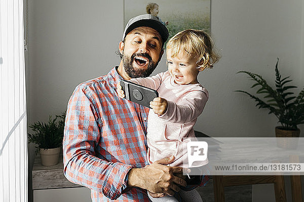 Vater hält seine kleine Tochter auf dem Arm und spielt mit seinem Smartphone