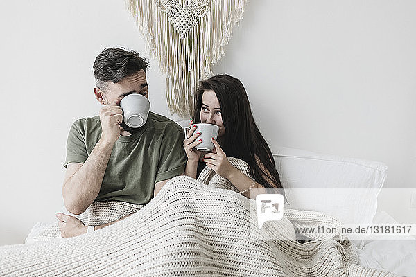 Glückliches Paar sitzt im Bett  trinkt Kaffee  hat Spaß