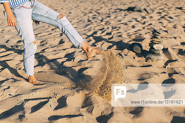 Frau steht auf einem Bein und wirft Sand an den Strand  Teilansicht
