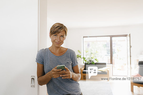 Porträt einer lächelnden Frau zu Hause mit Handy in der Hand