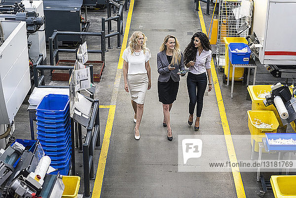 Three women with tablet walking and talking in factory shop floor