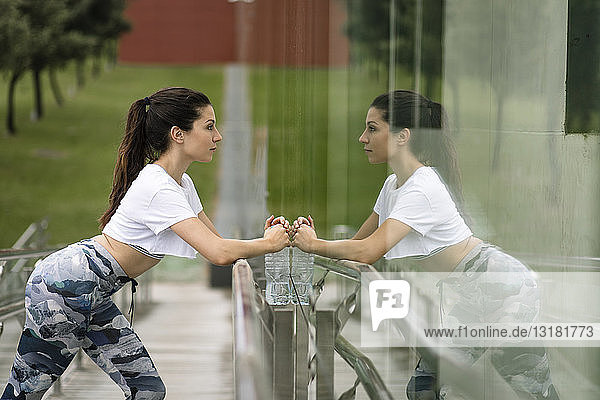 Junge Frau macht Dehnungsübung  die sich in Glasfassade spiegelt
