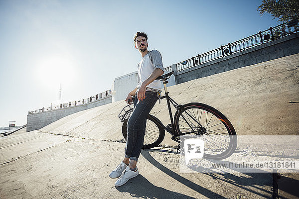 Junger Mann mit Pendler-Fixie-Fahrrad macht Pause an Betonmauer