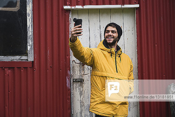 Junger Mann steht vor einer Wellblechhütte und nimmt Selfie