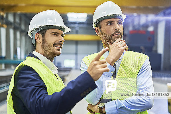 Two managers wearing protective workwear talking in factory