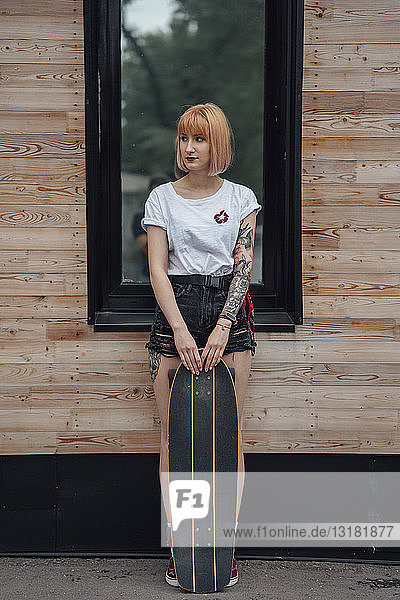 Junge Frau steht mit Carver-Skateboard vor dem Gebäude