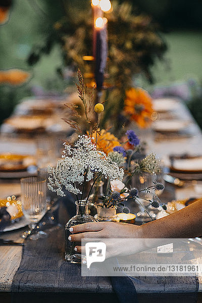 Hand placing flower vase on festive laid table with candles outdoors