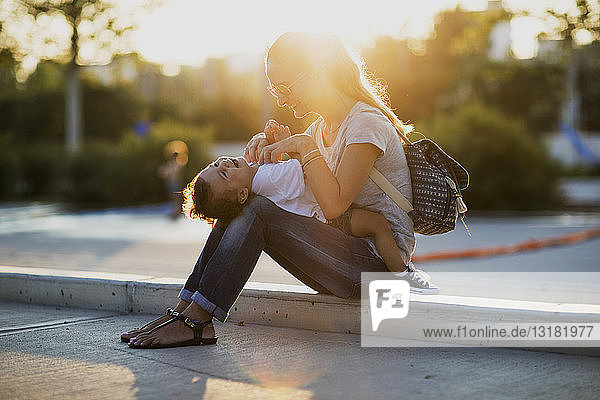 Happy mother playing with her little son on a square at sunset