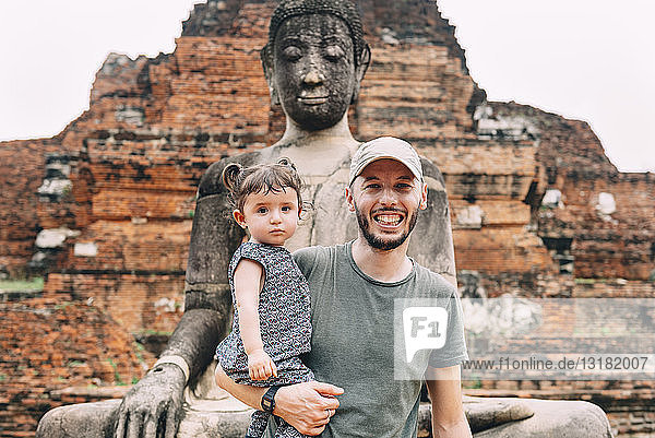 Thailand  Ayutthaya  Porträt eines lächelnden Vaters und einer lächelnden Tochter bei einer Buddha-Statue im Wat Mahathat