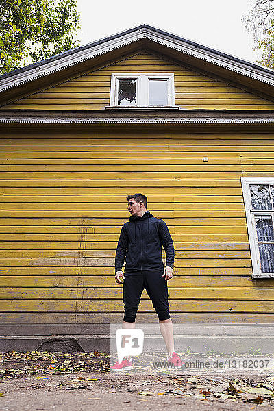 Sportler steht vor einem gelben Holzhaus