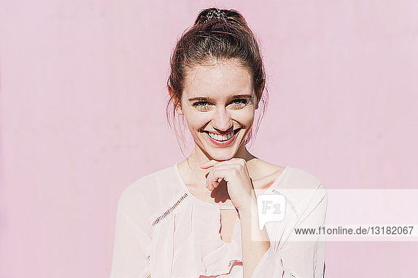 Porträt einer lächelnden jungen Frau vor rosa Wand