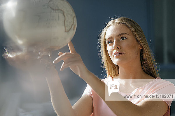 Porträt einer jungen Frau  die den Globus betrachtet und auf ihn zeigt