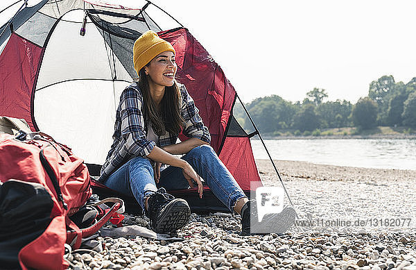 Glückliche junge Frau sitzt in einem Zelt am Flussufer