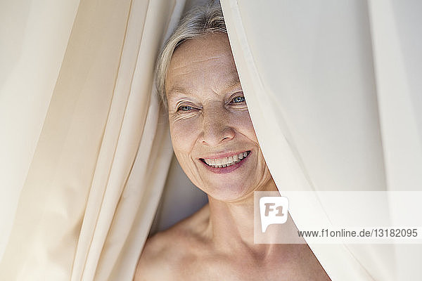 Porträt einer entspannten älteren Frau hinter dem Vorhang