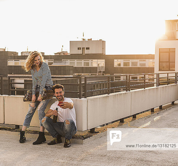 Junges Paar entspannt sich bei Sonnenuntergang auf der Dachterrasse und nimmt sich mit dem Handy ein