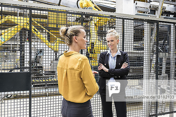 Two women talking in factory shop floor with industrial robot