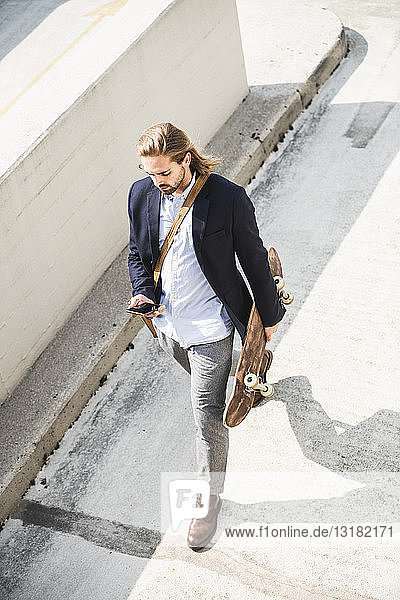 Young businessman carrying skateboard  using smartphone