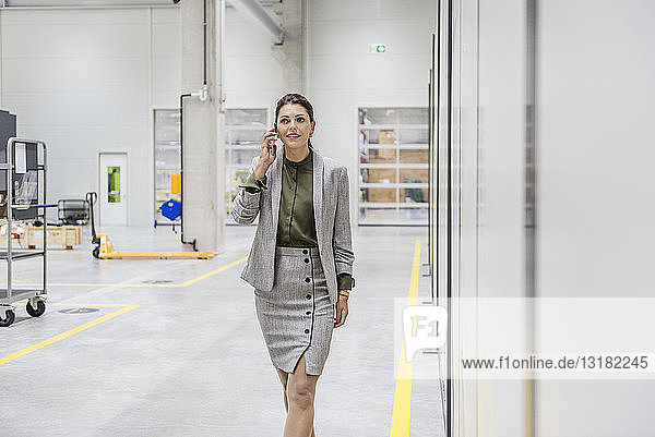 Businesswoman walking in factory workshop  talking on the phone
