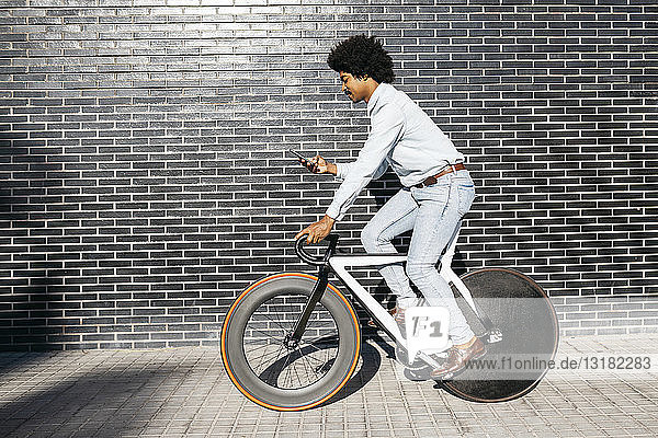 Mittelgroßer erwachsener Mann,  der Fahrrad fährt und ein Smartphone benutzt