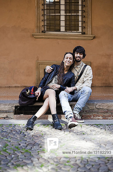 Porträt eines glücklichen jungen Paares  das auf Stufen im Freien sitzt