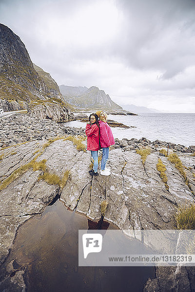 Norwegen  Lofoten  zwei Frauen in Regenjacken Rücken an Rücken auf einem Felsen stehend