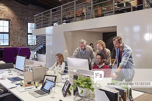 Kollegen schauen einem jungen Mann über die Schulter  der in einem modernen Büro arbeitet