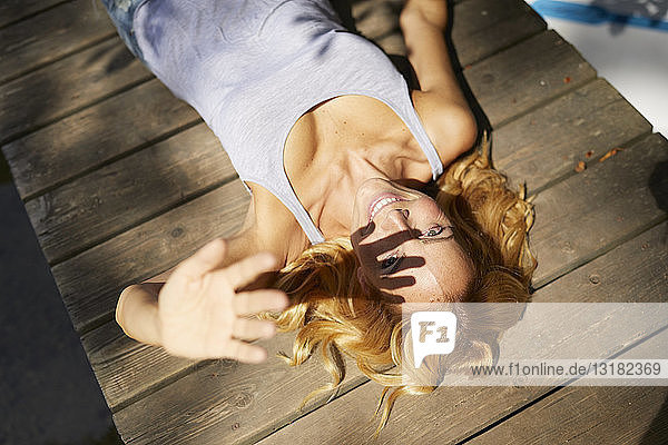 Glückliche blonde Frau liegt auf einem Holzsteg im Sonnenschein