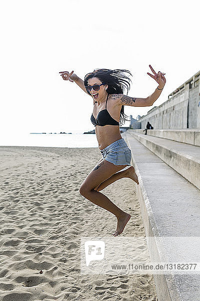 Porträt einer glücklichen jungen Frau  die auf den Strand springt