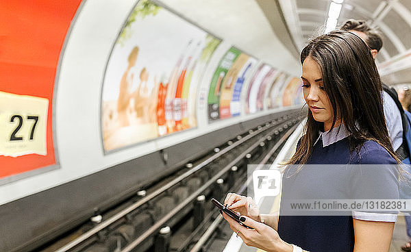 Großbritannien  London  junge Frau wartet am Bahnsteig der U-Bahn-Station und schaut auf ihr Handy
