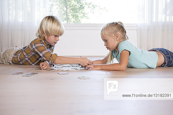 Bruder und Schwester liegen zu Hause auf dem Boden und spielen Puzzlespiele
