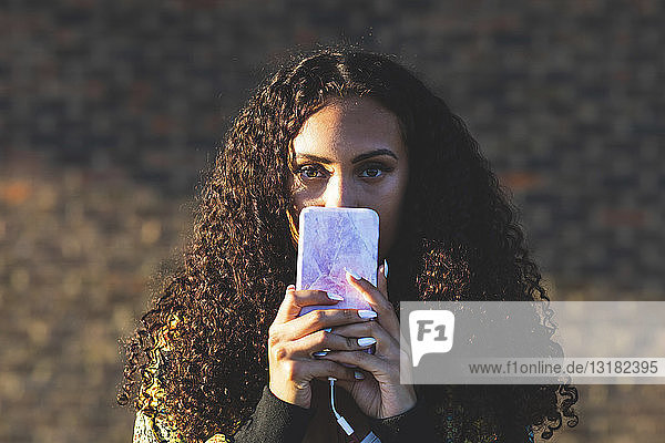 Porträt einer jungen Frau mit lockigem Haar  die ein Mobiltelefon hält