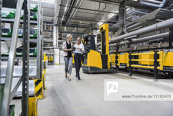 Two women with tablet walking and talking in factory shop floor