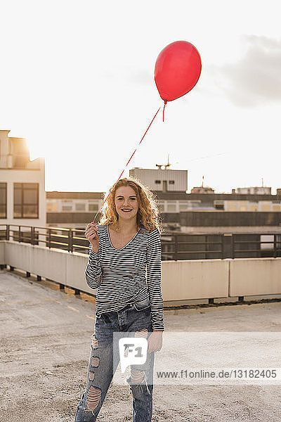Porträt einer jungen Frau mit rotem Ballon auf der Dachterrasse bei Sonnenuntergang