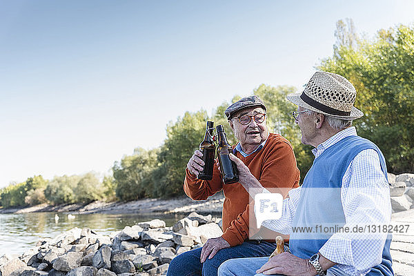 Alte Freunde sitzen am Flussufer und trinken Bier