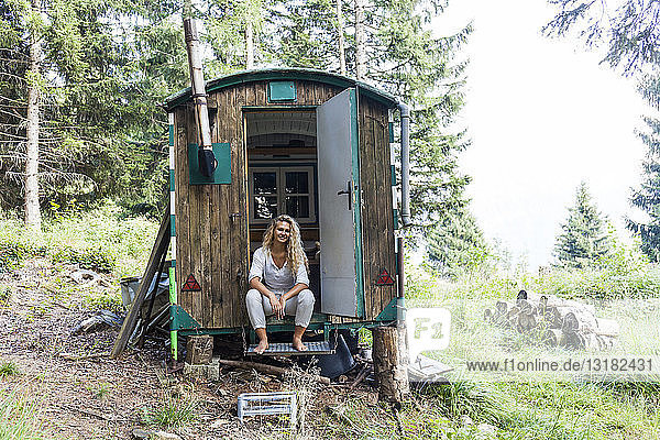 Deutschland  Bayern  Oberammergau  lächelnde junge Frau sitzt im Wohnwagen auf der Bergwiese