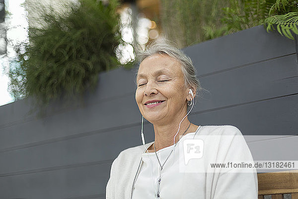 Smiling senior woman with closed eyes wearing earphones outdoors