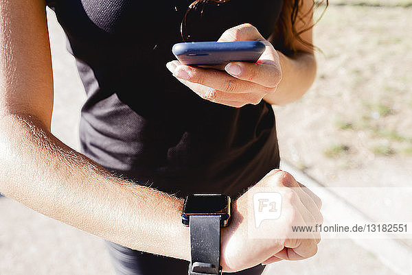 Close-up of sporty young woman using cell phone and smartwatch