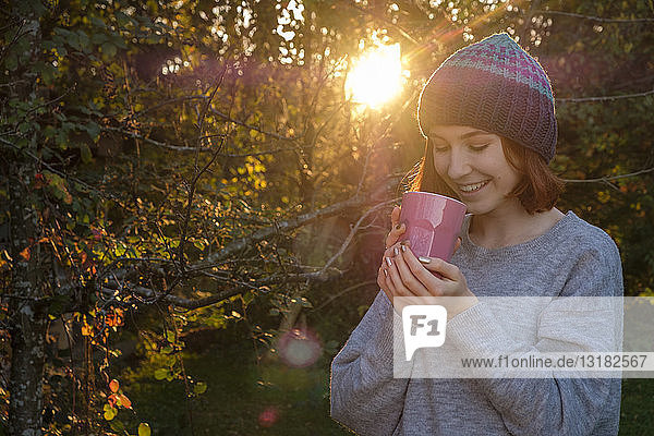 Porträt einer lächelnden Teenagerin  die im Herbst draußen Tee trinkt