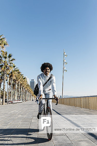 Mittelgroßer erwachsener Mann  der auf einer Strandpromenade Fahrrad fährt und Musik hört