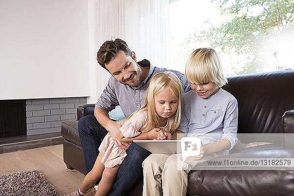 Vater und Sohn sitzen zu Hause auf der Couch und benutzen Tabletten