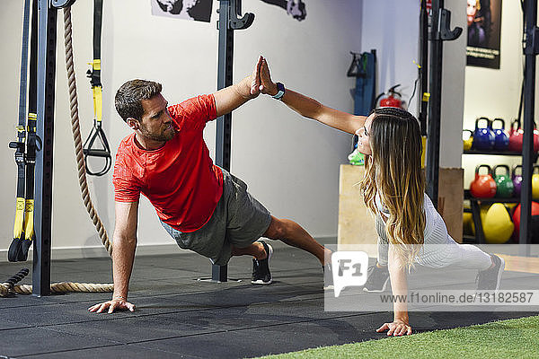 Couple exercising side plank with high-five in a gym