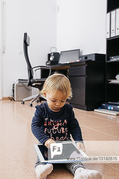Little girl sitting on the floor at home using tablet