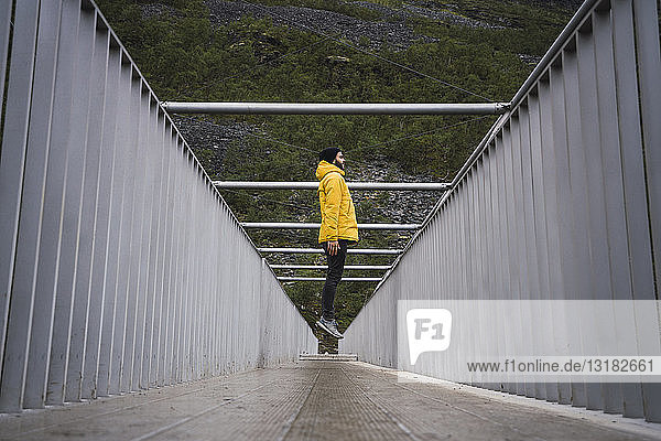 Junger Mann mit Regenmantel  der auf eine Brücke springt