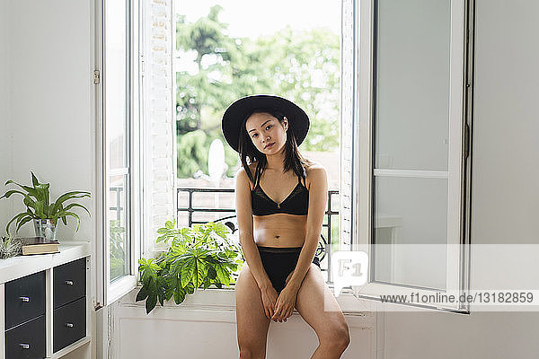 Portrait of attractive young woman wearing hat and lingerie sitting at the window