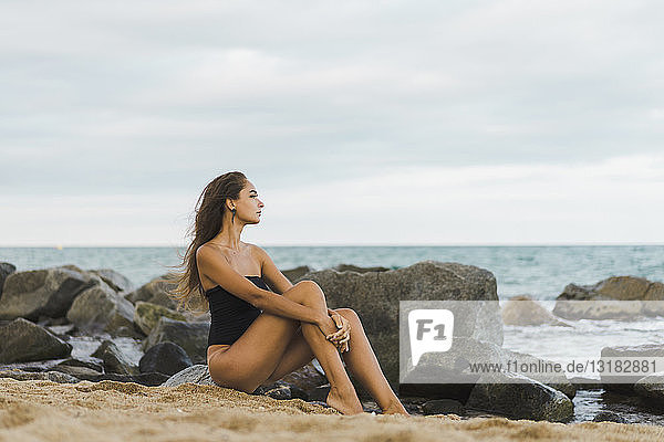 Hübsche junge Frau im Badeanzug am Strand sitzend