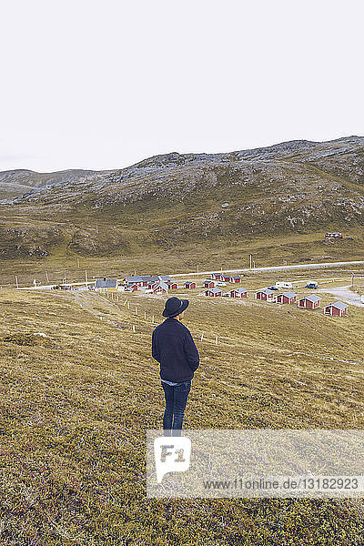 Junger Mann steht auf einem Hügel  schaut auf eine Siedlung  Nordkap  Norwegen