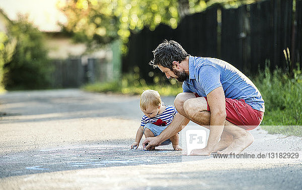 Vater und seine kleine Tochter malen im Sommer gemeinsam mit Kreide auf der Straße